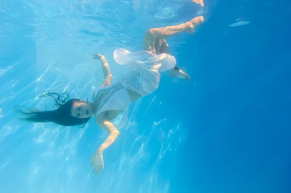 Nainen valkoisessa mekossa veden alla uima-altaassa — kuvapankkivalokuva