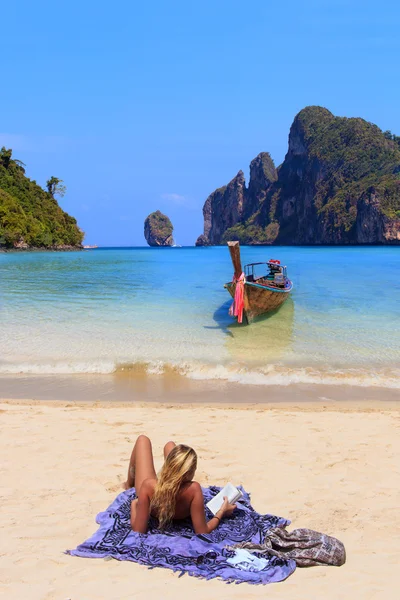 Unga blonda kvinnan läser en bok på stranden — Stockfoto