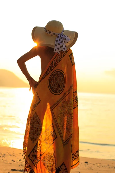 Kvinna i sarong på stranden vid soluppgång — Stockfoto