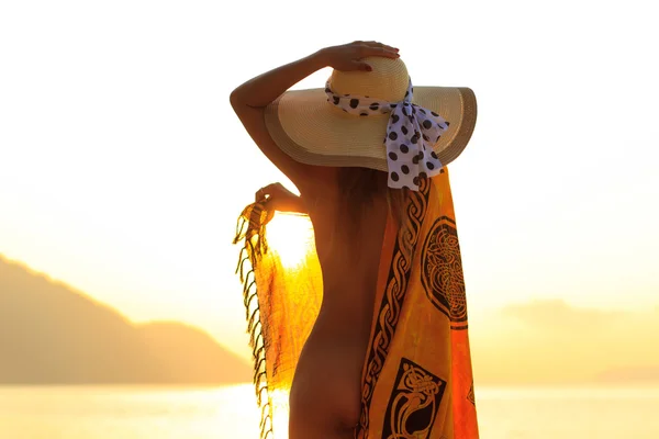 Kvinna i sarong på stranden vid soluppgång — Stockfoto
