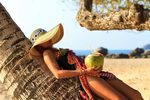 Женщина в саронге на кокосовом дереве с коктейлем на пляже — стоковое фото