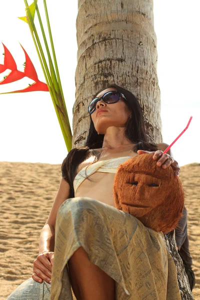 Vrouw in sarong op een kokosnoot boom op het strand — Stockfoto