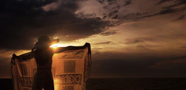 Vrouw in sarong op het strand bij zonsopgang — Stockfoto