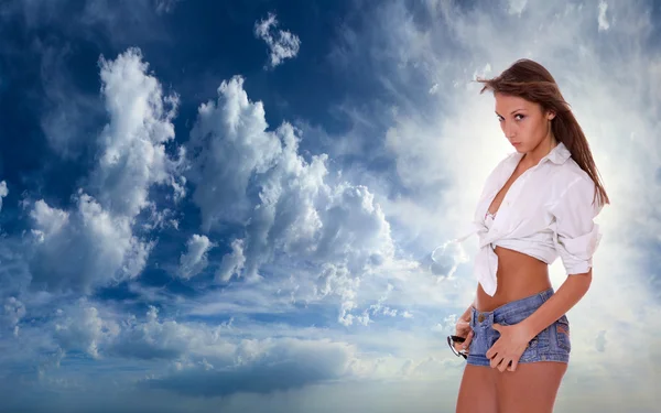 Жінка в джинсових шортах стоїть на блакитному хмарному небі — стокове фото