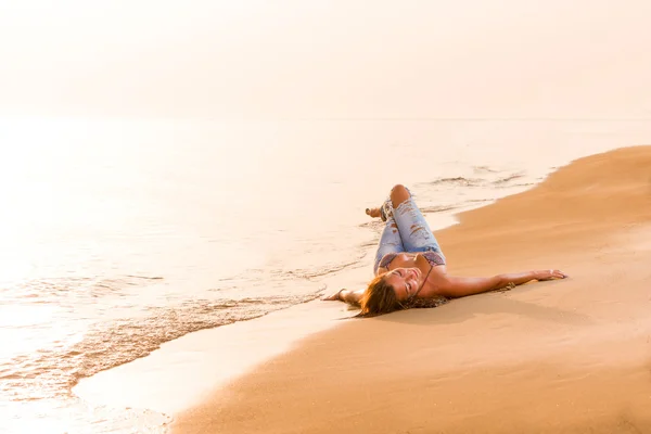 Modelo em jeans junto ao mar ao nascer do sol — Fotografia de Stock