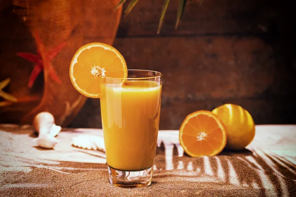 Glass of orange juice on a beach table — Stock Photo, Image