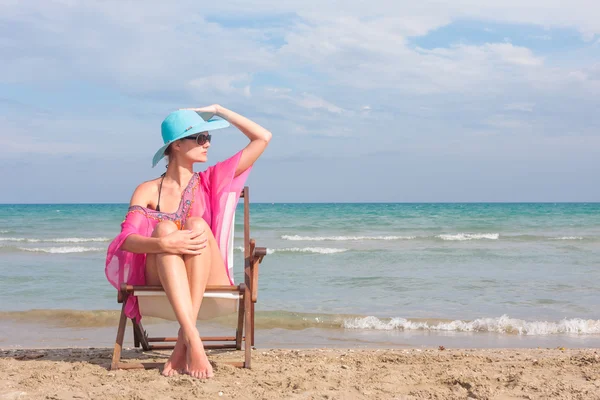 Flicka sitter på en stol på stranden — Stockfoto