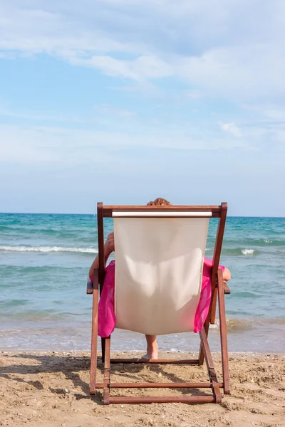 Meisje, zittend op een stoel op het strand — Stockfoto