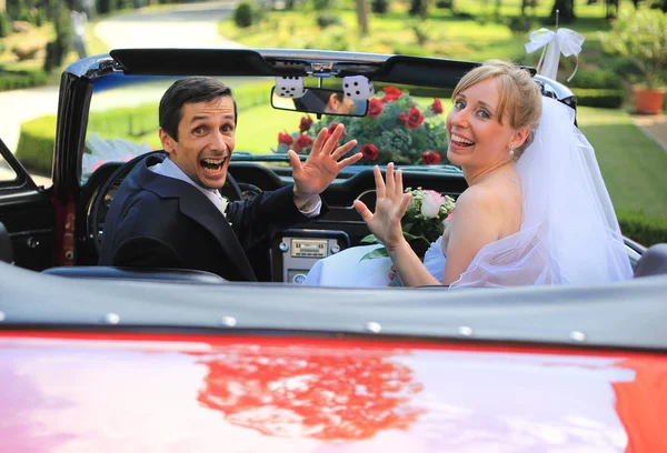 Young wedding couple waving in cabriolet car — Stock Photo, Image
