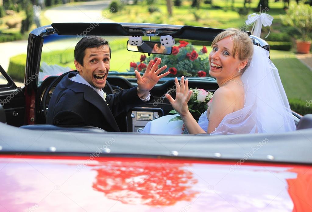 Young wedding couple waving in cabriolet car