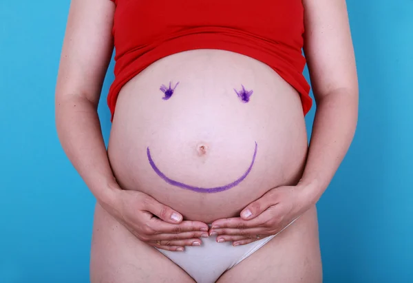 Mujer embarazada con la cara sonriente feliz pintado en el vientre — Foto de Stock