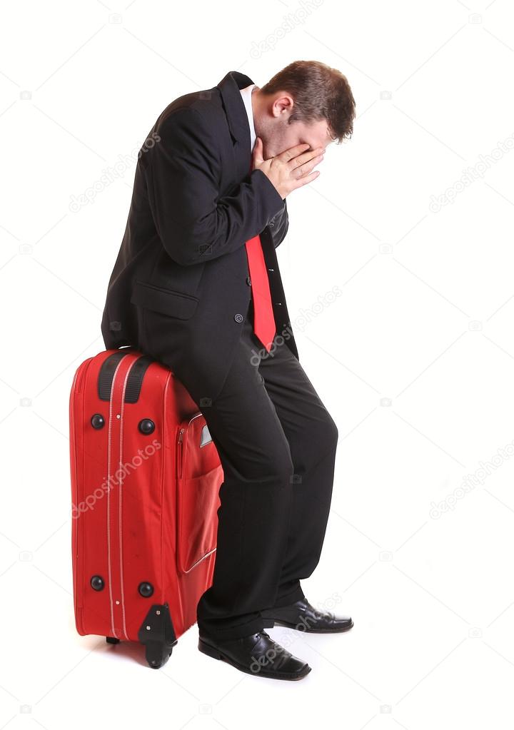 Worried businessman sitting on red luggage isolated on white
