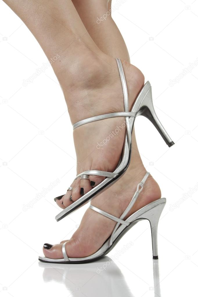Female feet wearing silver high heel shoes over white