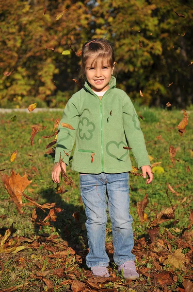 Söt liten flicka leker med löv i höstparken — Stockfoto