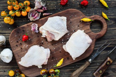 Ahşap bir kesim tahtasının üzerinde çiğ tavuk eti ve taze biber, domates ve İtalyan sarımsağı içerikli rustik bir arka plan..