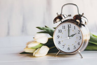 Daylight savings time concept. Set your clocks and to 2 am with this image of an alarm clock with white tulip flowers. Selective focus with blurred foreground and background with copy space.
