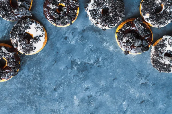 涂上蓝色纹理的背景上涂满了由黑白色巧克力 糖霜和碎屑的饼干做成的炸面圈 — 图库照片