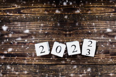 Ahşap beyaz takvim blokları yeni yıl 2022 'den 2023' e kadar dönüyor. Düşen karlı masa üstü görünümü.
