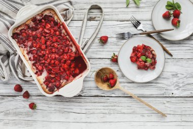 Yüksek açılı ev yapımı çilekli turta ya da kırmızı seramik bir tavada pişirilmiş Sonker 'ın çay tabağı, önlük ve ahşap bir tahta kaşıkla servis edilişi.. 