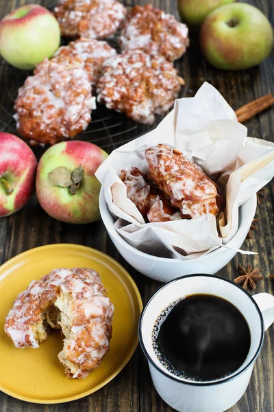 Glazed apple fritters and fresh hot steaming black coffee with fresh apples, cinnamon bark and anise. Top view.