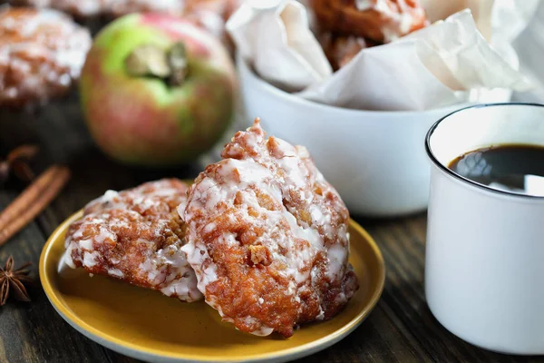 Glazed apple fritters and hot coffee with fresh apples, cinnamon bark and anise. Selective focus with blurred background.