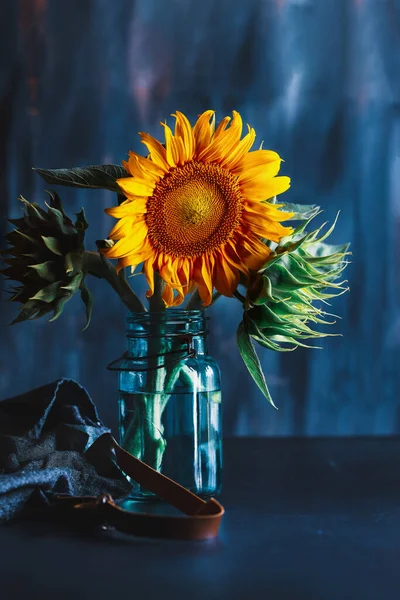 Bouquet of sunflowers in an antique blue mason jar with apron lying nearby. Selective focus with blurred background.