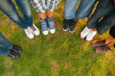 Legs and sneakers of teenage boys and girls standing in half circle on the grass
