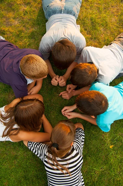 Zes tiener jongens en meisjes liggen in het gras op zonnige lentedag — Stockfoto