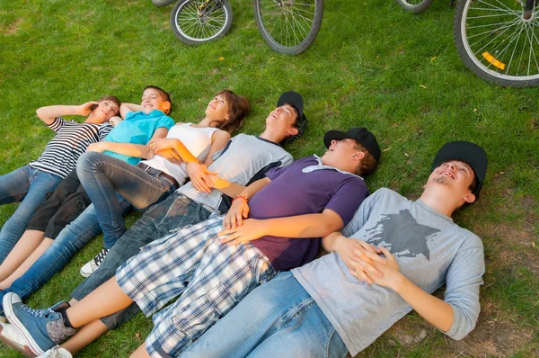 Ragazzi e ragazze adolescenti sdraiati sull'erba dopo aver cavalcato le biciclette — Foto Stock