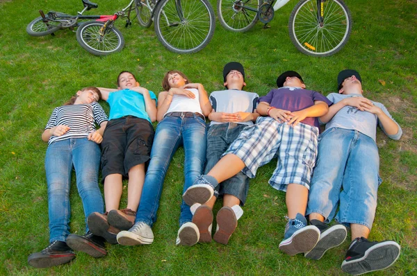 Adolescentes niños y niñas tumbados en la hierba después de montar en bicicleta — Foto de Stock