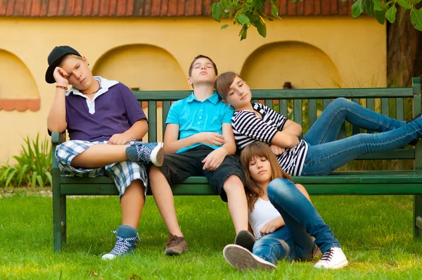 Gelangweilte Teenager sitzen und liegen auf der Bank an einem schönen Frühlingstag — Stockfoto