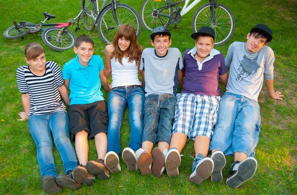 Gelukkig tiener jongens en meisjes rusten in het gras na paardrijden fietsen — Stockfoto