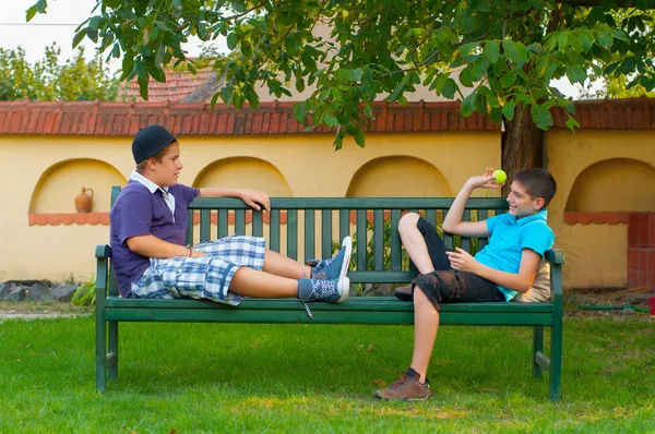 Due ragazzi adolescenti seduti sulla panchina e che si lanciano palla a vicenda — Foto Stock