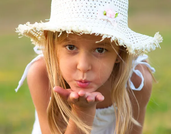 Cute little girl on the meadow blowing a kiss toward you on beautiful summer day — Stock Photo, Image