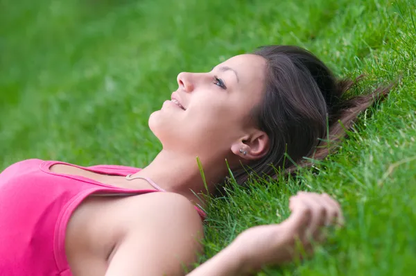 Mooi blij meisje liggend op het groene gras op een warme zomerdag — Stockfoto