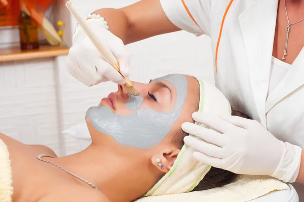 Mooie jonge vrouw liggend op een massagetafel terwijl gezichtsmasker is gezet op haar gezicht — Stockfoto