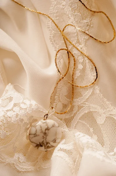 Golden necklace with semiprecious stone lying on white silk — Stock Photo, Image