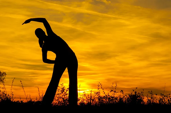 Silhouette of the slim girl stretching out in the nature at sunrise — Stock Photo, Image