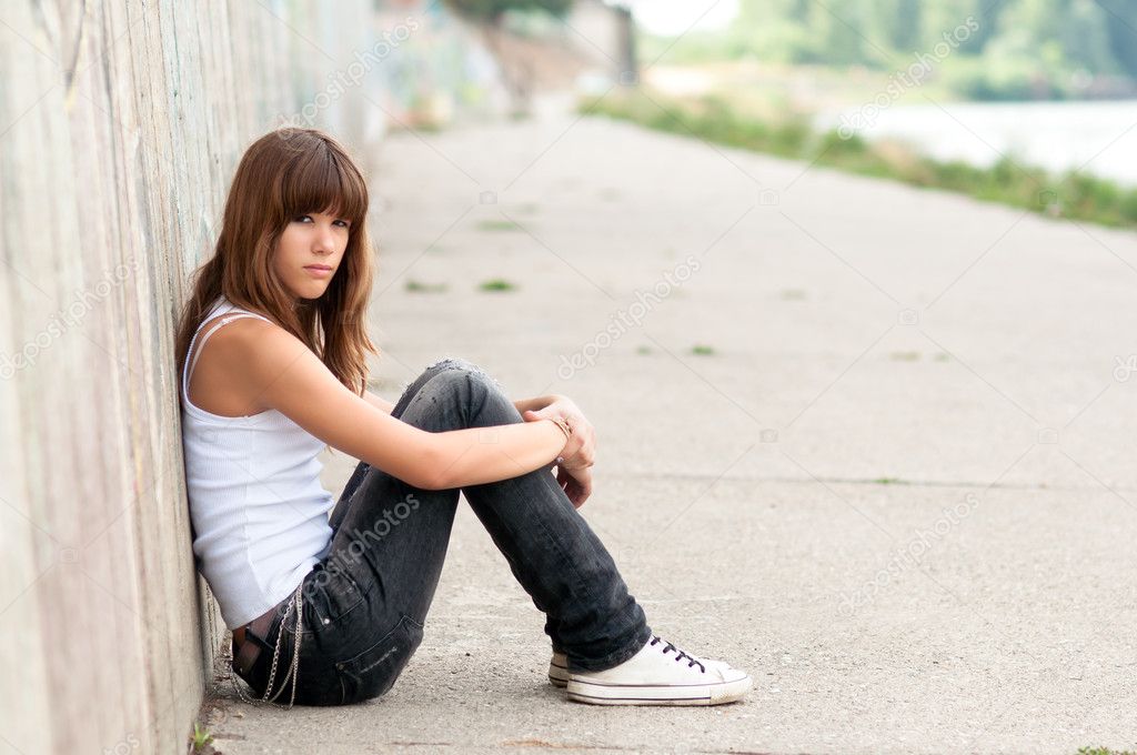 Cute sad teenage girl sitting alone in urban environment
