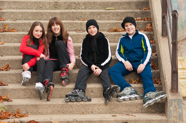 Group of happy teenagers in roller skates sitting on the stairs on beautiful autumn day