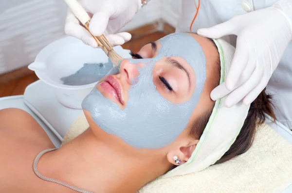 Beautiful young woman lying on massage table while facial mask is put on her face. — Stock Photo, Image