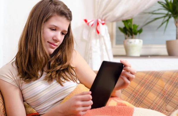 Cute teenage girl reading novels on ebook reader while sitting on the couch — Stock Photo, Image