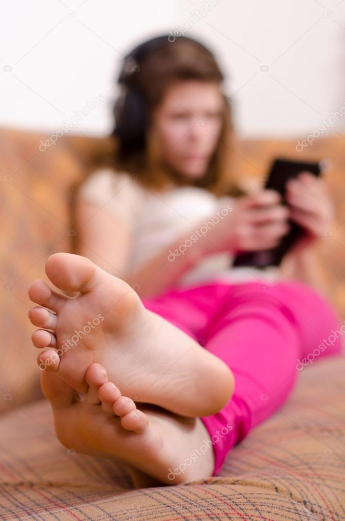 Cute teenage girl having fun with tablet pc while lying on the couch. Focus is on the feet