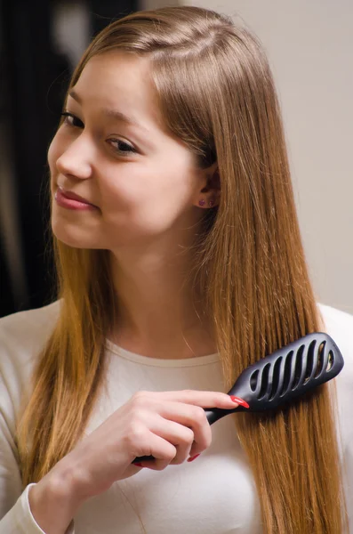 Beautiful smiling girl combing her hair in front of the mirror — Stock Photo, Image