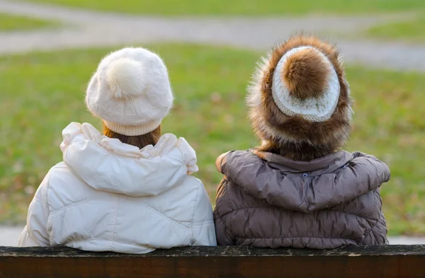 Twee meisjes zitten op de bank in het park — Stockfoto
