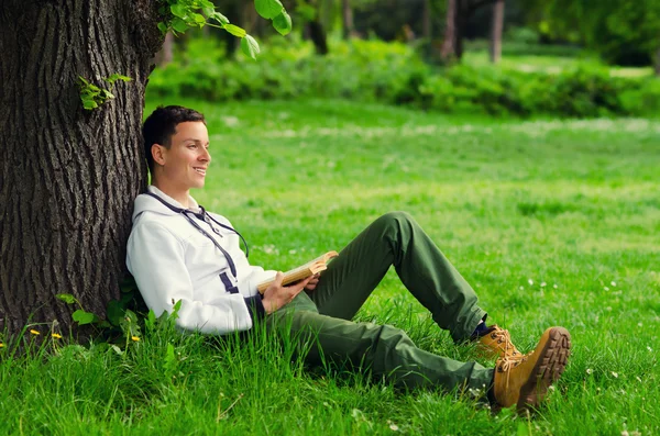 Junger glücklicher Mann liest Buch in der Natur — Stockfoto