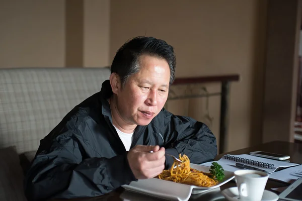 Keski-ikäinen mies syö nuudeleita — kuvapankkivalokuva