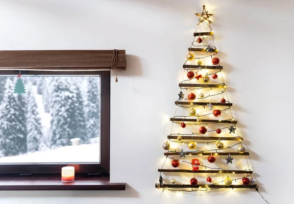 Arbre de Noël en bois suspendu au mur, paysage enneigé d'hiver devant la fenêtre. — Photo