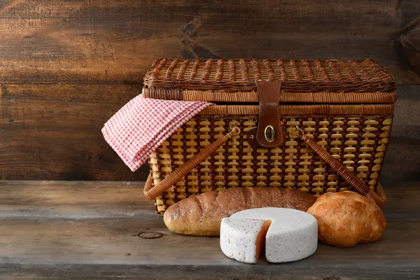 Picnic basket with bread and cheese on wood — Stock Photo, Image