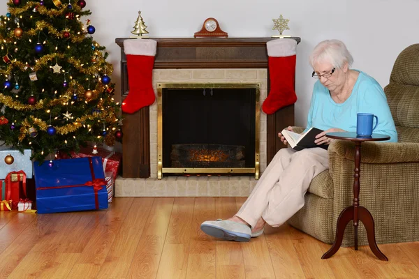 Äldre kvinna läsa bok i jul vardagsrum — Stockfoto